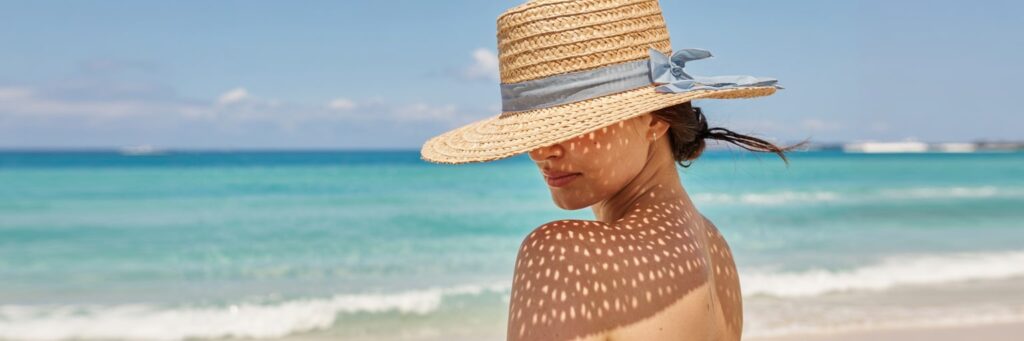 Frau mit Sonnenhut am Meer schützt ihre Haut vor direkter Sonne nach dem Lasern