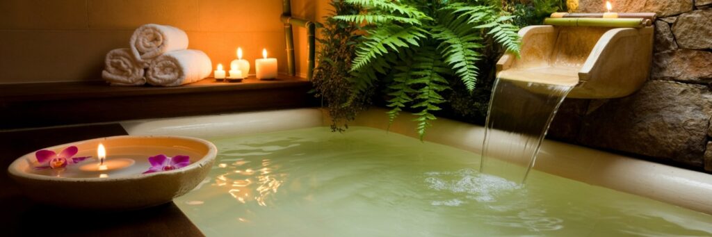 Stimmungsvolles Spa-Ambiente mit warmem Licht, Wasserbecken, brennenden Kerzen und Handtüchern für eine entspannte Behandlungen-Atmosphäre