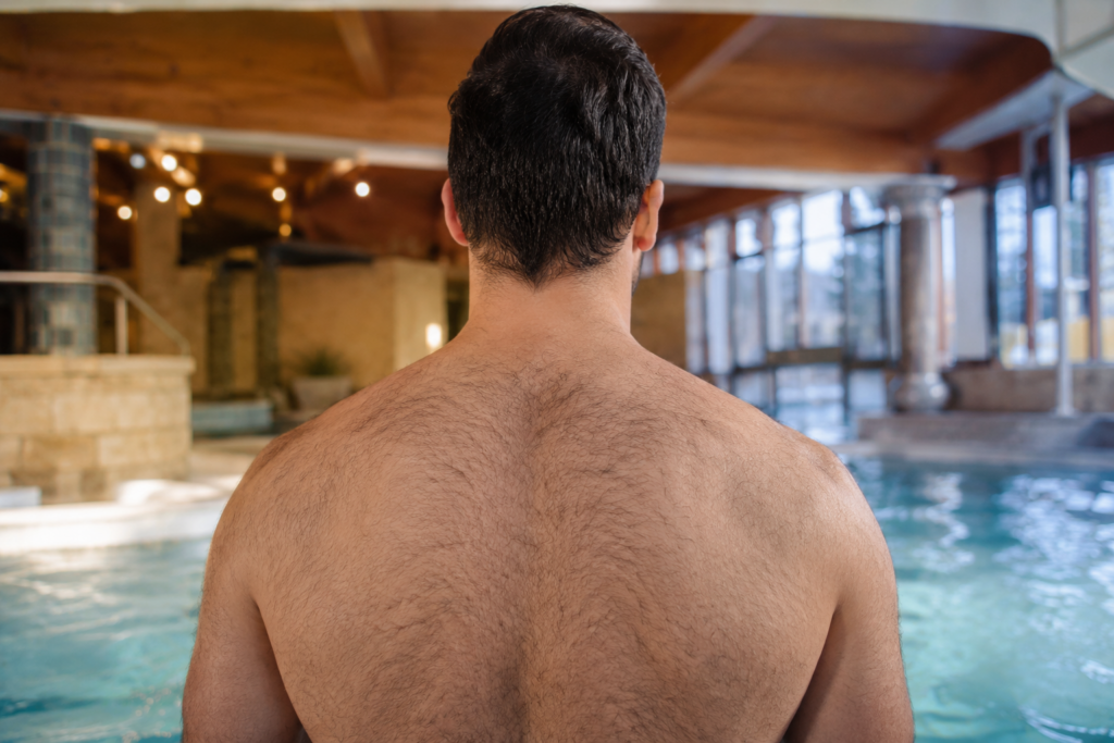 Mann mit Rückenhaaren vor einem Wellness- und Thermenbereich.
